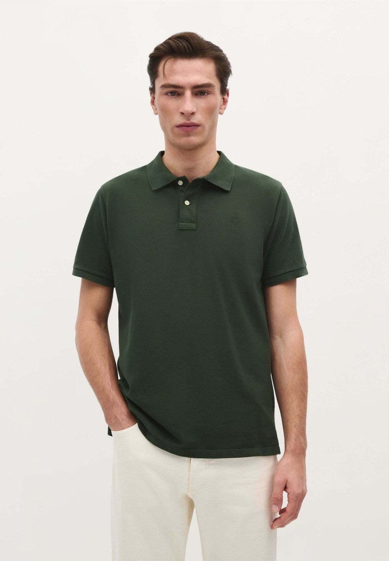Camisa polo verde oscuro de algodón con cuello, dos botones y mangas cortas. Presenta un logotipo sutil y una textura lisa.
