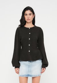 Πλεκτή σκούρα καφέ ζακέτα με στρογγυλή λαιμόκοψη, μακριά φουσκωτά μανίκια και κλείσιμο μπροστά με κουμπιά ανοιχτού χρώματος.