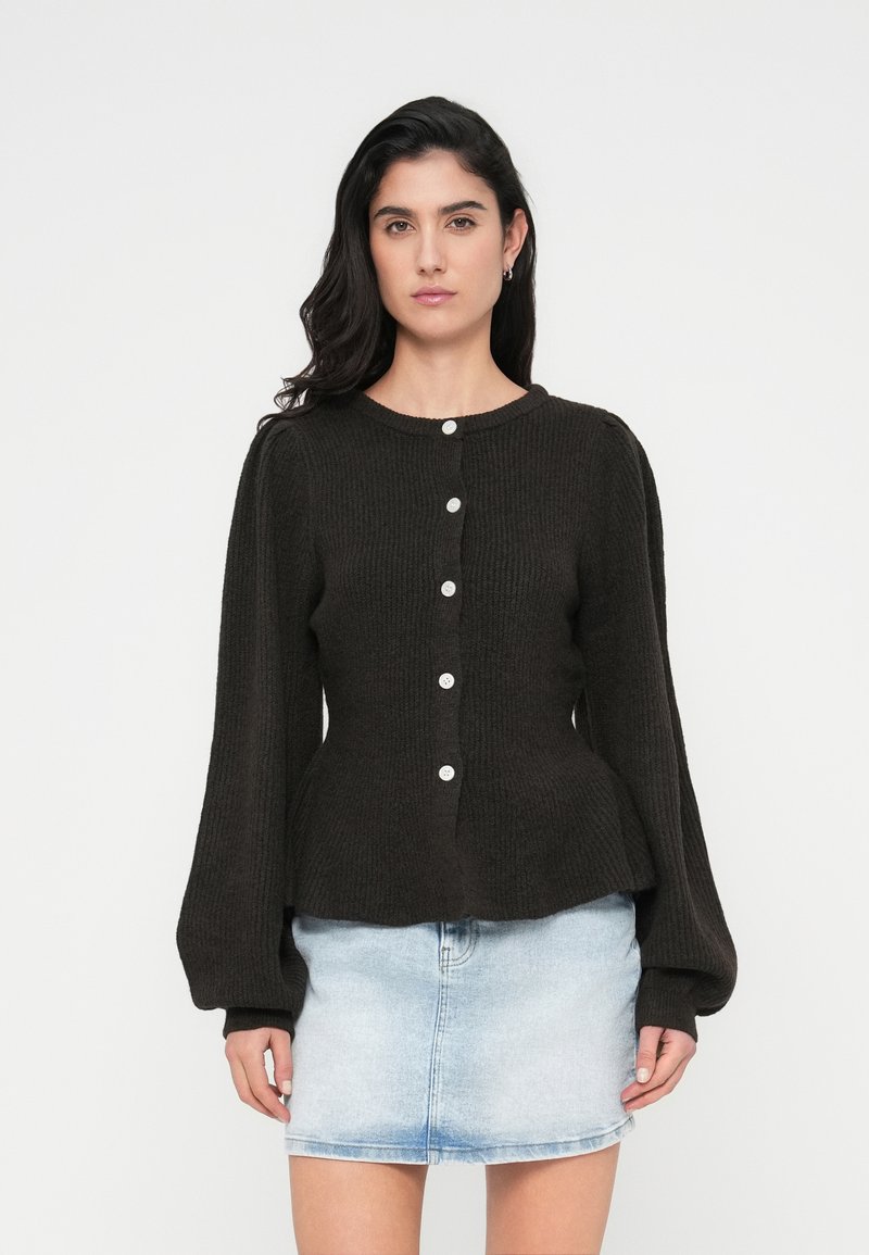 Πλεκτή σκούρα καφέ ζακέτα με στρογγυλή λαιμόκοψη, μακριά φουσκωτά μανίκια και κλείσιμο μπροστά με κουμπιά ανοιχτού χρώματος.