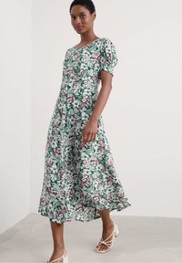 Floral dress featuring green, pink, and white colors with puffed sleeves. Knee-length, relaxed fit, made of light fabric with a smooth texture.