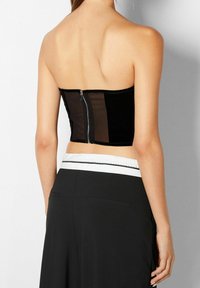 Musta olkaimeton yläosa, jossa on vartalonmyötäinen leikkaus, samettinen tekstuuri ja vetoketjusuljin takana, yhdistetty korkeavyötäröisiin mustiin housuihin.