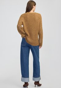 Brązowy sweter z dzianiny o luźnym kroju, z teksturowanym wzorem. Połączony z niebieskimi spodniami o wysokim stanie i szerokich nogawkach oraz brązowymi botkami na obcasie.