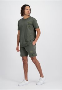 Zestaw oliwkowozielonej bawełnianej koszulki i szortów z detalami kieszeni na przodzie, dopasowanego materiału oraz białych sneakersów. Prosty design z luźnym krojem.
