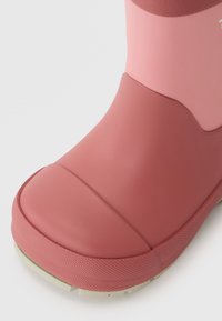 Stivaletto in gomma rosa con superficie liscia, punta rotonda, dettagli testurizzati sulla suola e suola esterna di un verde chiaro a contrasto.