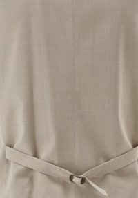 Beige Kleidungsstück aus strukturiertem Stoff, mit einer taillierten Passform, die durch einen Stoffgürtel gesichert ist. Schlichtes Design ohne Verzierungen.