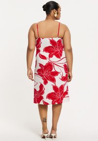 Robe d'été à imprimé floral rouge avec des fines bretelles, design mi-long, fond blanc, tissu lisse, présentant de grands motifs d'hibiscus rouges.