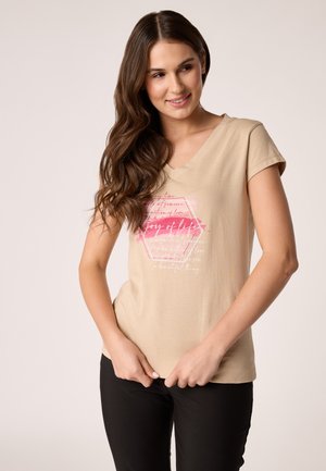 Beige v-neck t-shirt with short sleeves, featuring a pink and white graphic print with text. Soft fabric, fitted design, styled with black pants.
