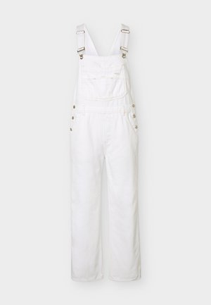 Λευκή τζιν σαλοπέτα με ρυθμιζόμενους ιμάντες στους ώμους, μπροστινή τσέπη στο στήθος, πλαϊνά κουμπιά και φαρδιά, ίσια πόδια, εμφανίζεται σε απλό φόντο.