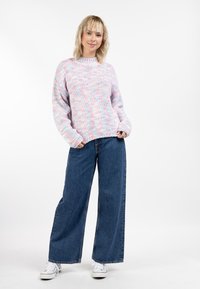 Strickpullover mit einem Pastellfarbmix, Rundhalsausschnitt und weiten Ärmeln, kombiniert mit locker sitzenden dunkelblauen Jeans und weißen Turnschuhen.