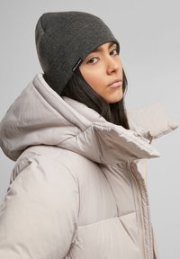 Gray knit beanie and light beige puffer jacket with a high collar. Puffer jacket has a quilted texture and a zippered front.