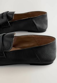 Black leather slip-on loafers with penny strap detail and brown interior lining, shown from a side angle on a light background.
