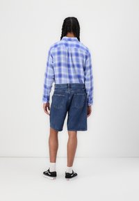 Blue and white plaid long-sleeve shirt with button cuffs, paired with denim shorts. Black shoes with white soles and visible socks.