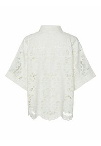 Vit spetsblus med blommönster i utskärning, korta ärmar, krage och vågig nederkant, som visar upp en intrikat textur och design.
