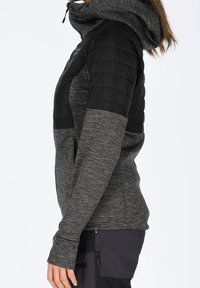 Czarna i szara hybrydowa kurtka z kapturem na zamek, z pikowanymi czarnymi ramionami i teksturowanym szarym korpusem. Długie rękawy z otworami na kciuki.