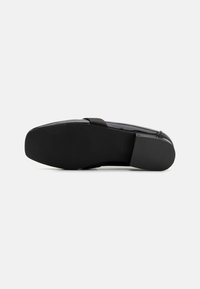 Zapato plano negro con un elegante upper de piel sintética, punta redondeada y suela de goma texturizada para agarre. Presenta un diseño minimalista.