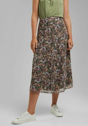 Woman wearing a floral midi skirt with small pink, white, and blue flowers, paired with white sneakers and a green sleeveless top.