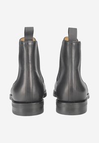 Schwarze Chelsea-Stiefel aus Leder mit elastischen Seitenteilen, flachen Sohlen und Zuglaschen an der Rückseite für einfaches An- und Ausziehen, die eine glatte Textur und ein schlankes Design zeigen.