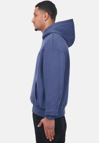 Blaue Baumwollkapuzenjacke mit einer Fronttasche, Kordelzugkapuze und gerippten Bündchen. Der Stoff hat eine glatte Textur und einen lockeren Schnitt.