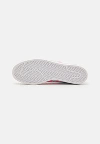 Sneaker sole in white rubber with a zigzag traction pattern; pink accents along the edge; smooth surface with a slight curve at the heel.