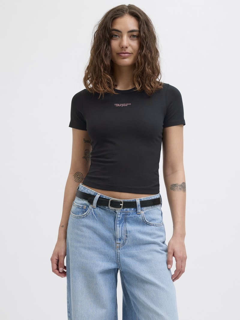 Schwarzes Baumwoll-T-Shirt mit kurzen Ärmeln in figurbetonter Passform und kleinem Text-Logo auf der Brust, kombiniert mit hellblauen, weit geschnittenen Jeans und einem schwarzen Gürtel.
