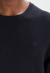 Jersey de punto azul marino con cuello redondo, que presenta un pequeño logo bordado en el pecho. Tejido suave y de peso medio.