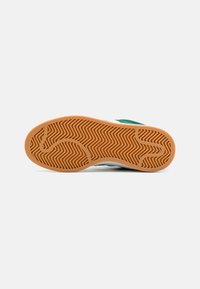 Semelle de sneaker avec un design texturé et à motifs en caoutchouc. Présente une structure flexible et une couleur brun clair, gomme.