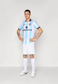 Fotbollströja med ljusblå och vita vertikala ränder, svarta detaljer och logotyp. Matchas med vita shorts och strumpor samt svarta fotbollsskor.