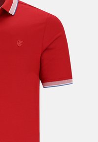 Röd polo med en texturerad väv, en klassisk krage med blå och vit trim, och en liten logotyp på bröstet.