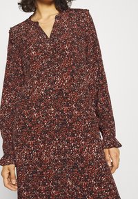 Vestido de manga larga con estampado floral en rojo y negro, fabricado en un material ligero, que cuenta con un cierre frontal de botones y puños con volantes.