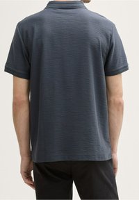 Polo gris foncé en tissu texturé, col plié et manches courtes. Manches ourlées et coupe droite.