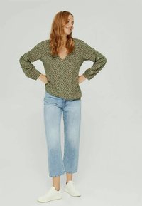 Haut vert à manches longues avec un motif léopard et un col en V, associé à un jean large bleu clair et des baskets blanches.