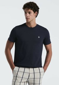 Marineblauwe katoenen T-shirt met een ronde hals en korte mouwen, voorzien van een klein wit logo geborduurd op de borst.