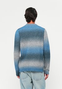 Pull en dégradé bleu et gris, texture tricotée, col rond, ourlet et poignets côtelés, porté avec un jean bleu clair.