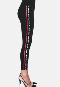 Czarne legginsy z białym i czerwonym paskiem po boku, wykonane z elastycznego materiału. Połączone z czarnymi szpilkami w szpic. Charakteryzują się dopasowanym krojem.