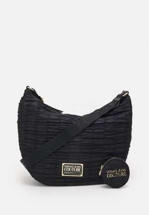 Czarna pikowana torebka na ramię z regulowanym paskiem, złotą plakietką z logo oraz przymocowaną małą okrągłą sakiewką na monety, marki "Versace Jeans Couture."