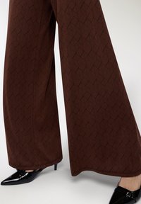 Pantaloni marroni a gamba ampia caratterizzati da un motivo geometrico di foglie in un tessuto testurizzato, abbinati a tacchi a punta neri.