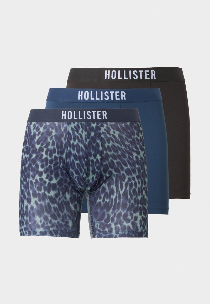 Τρία ανδρικά μπόξερ Hollister τοποθετημένα από μπροστά προς πίσω, με σχεδιασμούς σε μαύρο, μονόχρωμο μπλε και μπλε λεοπάρ φανέλα με λευκές ζώνες μέσης με λογότυπο.