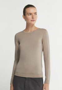 Beżowy sweter z długim rękawem, okrągłym dekoltem, dopasowanym krojem, cienkim splotem oraz ribbami na mankietach i dolnej krawędzi. Brak widocznych wzorów lub akcentów.