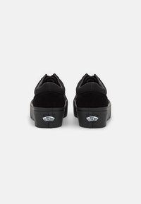 Sorte ruskind- og canvas sneakers med flad gummisål, afrundet tå og mærket hælaccent. Bagfra ses det minimalistiske design.