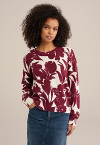 Burgundijas krāsas ziedu raksta adīta jakas ar garām piedurknēm un apaļu kakla izgriezumu, apvienota ar denima svārkiem. Iezīmē ribotu piedurknu un apakšmalu.