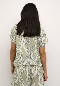 Haut vert clair à manches courtes avec des motifs abstraits en noir et blanc. Le tissu semble doux avec une coupe décontractée, associé à un bas assorti.
