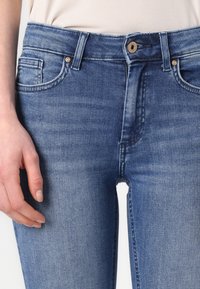 Tmavomodré džíny z denimu s priliehavým strihom, päťvreckovým štýlom a kovovým gombíkom na zapínanie, s jemnou textúrou a miernym vyblednutím.