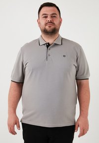 Szürke póló, rövid ujjal, fekete gallérral és részletekkel. Textúrált anyagból készült, háromgombos kivágással.