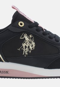 Mustat tennarit, joissa on nahkainen yläosa ja kultainen polo-pelaajan logo. Koristeina pinkit nauhat ja valkoinen pohja, jossa on pinkki raita.