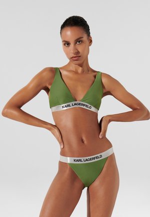 Zeleni bikini komplet, ki vključuje trikotno braletko in usklajene tangice. Oblikovanje vključuje srebrno logotipno elastiko in gladek, elastičen material.