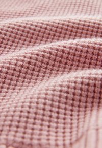 Tissu rose doux avec un motif en relief de type gaufre et de douces plis en gros plan.