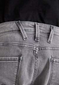 Vaqueros de mezclilla gris con una cinturilla de altura media, diseño de cinco bolsillos y detalle de costura a contraste. Textura suave y forma ajustada.