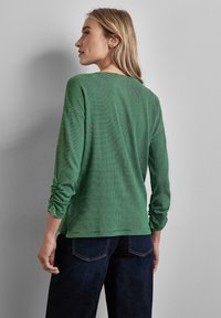 Groene en zwarte gestreepte blouse met lange mouwen en een ontspannen pasvorm. Heeft een ronde halslijn en opgerolde mouwen, gemaakt van zachte stof.