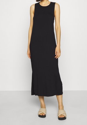 Black sleeveless midi dress with a rounded neckline, smooth texture, and a subtle side slit. Worn with beige crossed strap sandals.