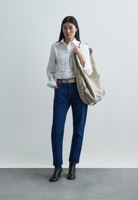 Fehér galléros ing, kék farmernadrág, fekete bokacsizma és egy arany díszítésű bézs válltáska. Az öv fémes logóval díszített.